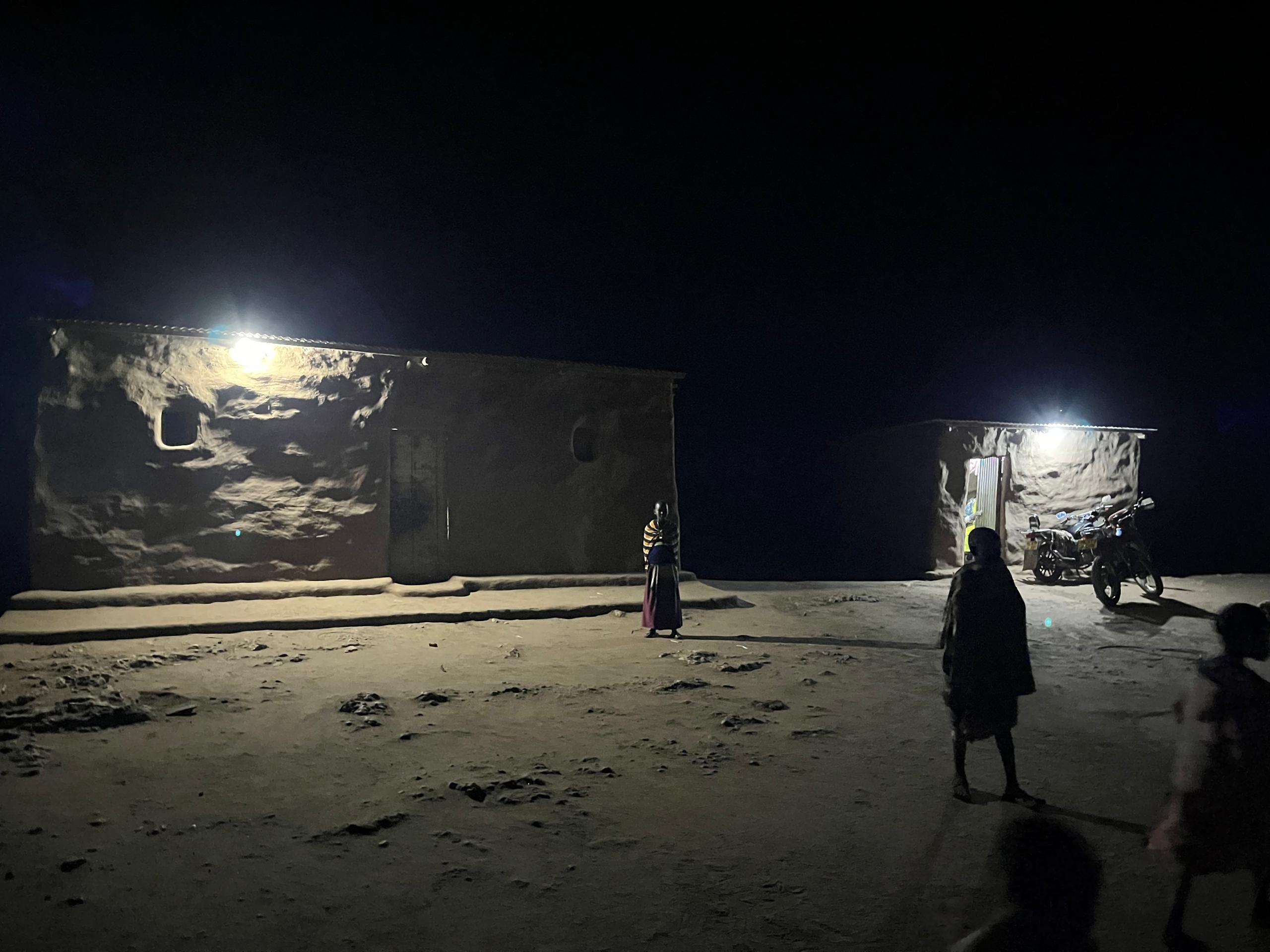 Two distant buildings are brightly illuminated by electric lights at night, showing the impact of the microgrid project.